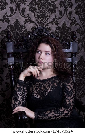 young beautiful woman in the black lace dress sit in the wood armchair
