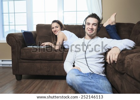 A woman lay on the sofa with laptop and a man ear music