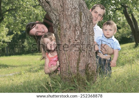A Smiling family standing behind a tree