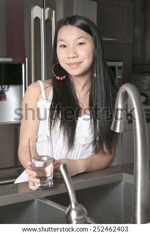 A teenager girl drinking water in the kitchen