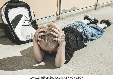 A very sad boy lay on the ground seam to be bullying in school playground.