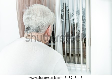 An Old and lonely lady looking outside through her window