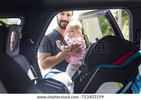 father putting his baby daughter into her car seat in the car