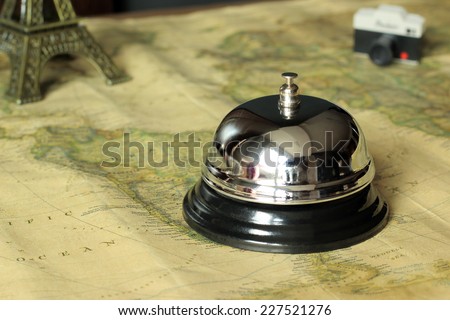Hotel service bell on a world map in a vintage decorate with a camera and a monument on the background. Travel and accommodation concept.