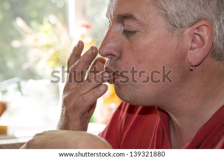 A grey haired man in profile licking his fingers while eating
