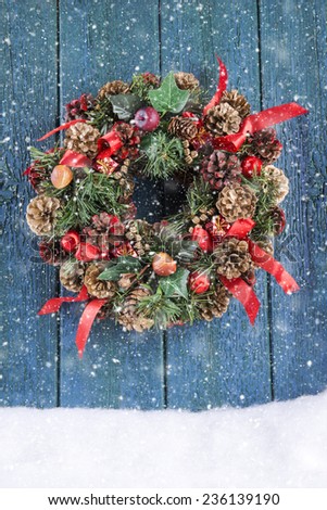 Christmas wreath on a green rustic door with falling snow
