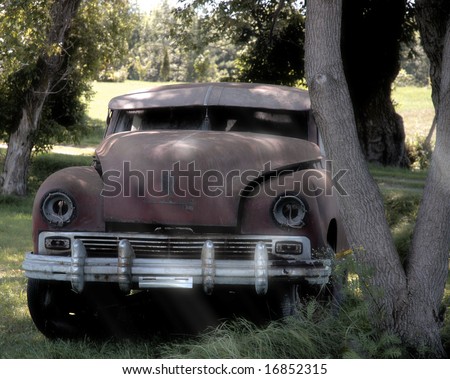 An old car resting by a tree with sun-rays shining upon it