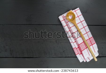 Wooden spoon and dish cloth on black wooden background.