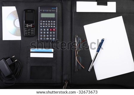Black business briefcase open wide with various office, computing and communication stuff inside, top view