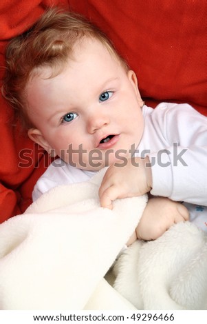 Baby girl lying on red sofa holding white blanket