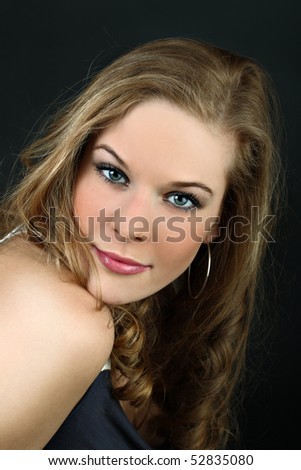 Beautiful girl with tilted head looks at camera on black background