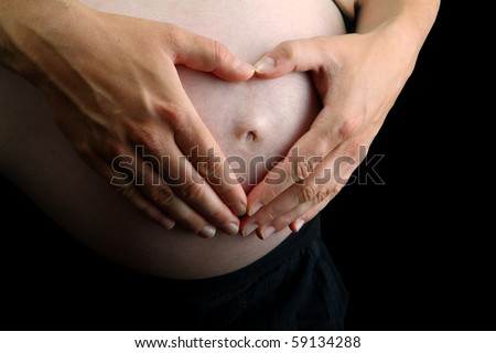 Two hands make a heart shape on beautiful pregnant belly on black background