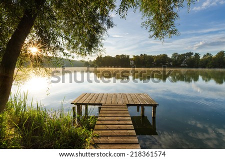 A wooden jetty at lake Wesslinger See at sunrise with sunstar