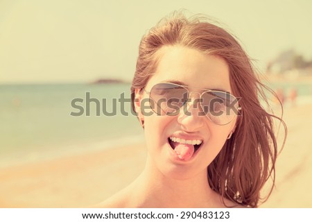 Retro Effect Of Portrait Happy Young Woman Portrait Sticking Out Tongue On Beach