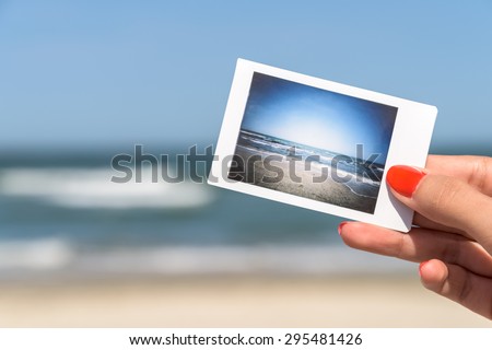 Girl Hand Holding Instant Photo Of Sea Beach Landscape, focus on hand
