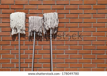three white mops lean against red brick wall revealed to sunlight exposure, brick wall background