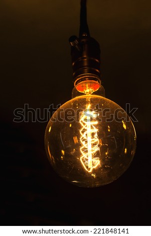 glowing round bulb tungsten lamp, heated filament light, incandescent illumination on dark background