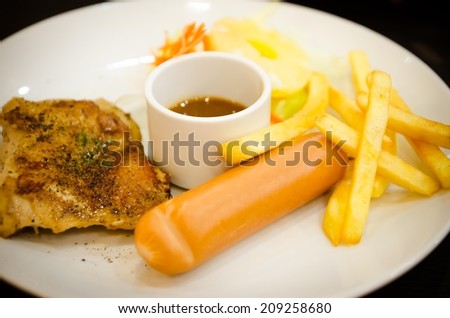 Grilled chicken steaks, sausage, French fries and vegetables