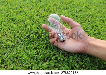 Energy saving concept. Hand holding light bulb on green grass background,.
