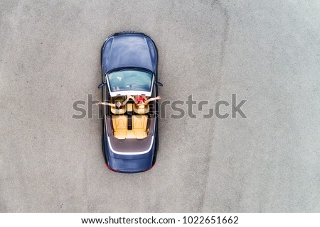 Small passenger sports convertible car with soft top down and happy couple of young women enjoying lifestyle and freedom in aerial top down view.