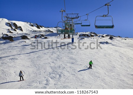 Snowy mountains chair lift up to the top of mountain at winter with white show and skiing ski resort snowboarders
