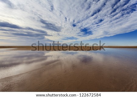fresh water shallow lake transparent sandy bottom with cloudy blue sky reflection at horizon vast area sea shore