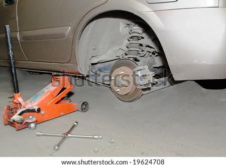 passenger car on technical maintenance service without unmounted rear wheel on jack with wrench