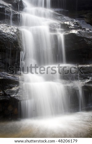 Waterfall cold fresh water stream long shutter speed blurred motion on black stone rocks in park