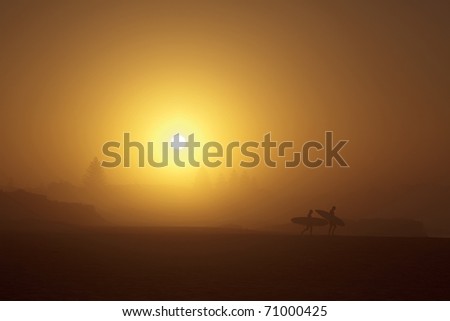 Earlier morning sunrise gold sun light colour silhouette of two surfers walking along beach
