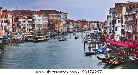 Italy Venice island grand canal view from Rialto Bridge along water flow with gondolas, pier, cafes, houses, attractions and other tourism services day time panoramic horisontal cityscape