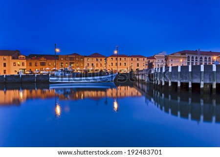 Australia Hobart city historic houses at water edge at sunset illuminated with reflection in still harbour water and fishing boat at jetty