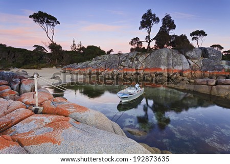 Bay of Fires red rocks around still lagoon with single small motorboat moored overnight on the rope reflecting in clear sea waters