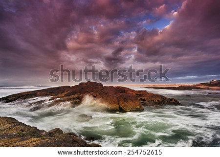 Ocean beach of rocks and sand at sunrise with stormy cloudy weather when first sun rays shed light on wet rocks