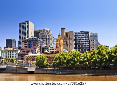 Melbourne city CBD cityline at Yarra river with greet trees and yellow river waters under blue sky