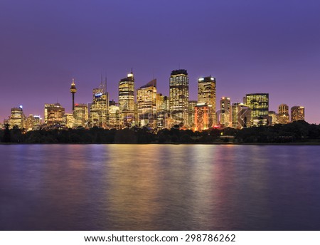 SYdney city CBD view from Royal Botanic Garden at sunset when skyscraper illumination is full on and bright lights reflecting in blurred still waters of Sydney Harbour
