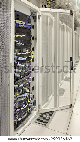 vertical rack of telecom and server equipment with opened cabinet's door in computer data centre