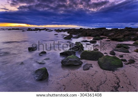 ocean beach of yellow sand and moss covered stones at sunrise in Sydney, Australia, pacific ocean