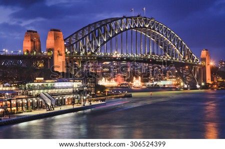 Australian Sydney Harbour bridge side view at sunset from Circular quay highly illuminated with lights reflecting in blurred harbour waters