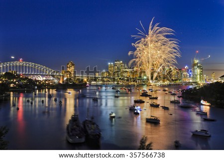 New Year eve fireworks in Sydney over Harbour towards CBD high-rises at sunset when sky is still blue and first light balls are bright