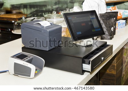 POS terminal consisting of Tablet computer with touchscreen, mobile printer and pay terminal on a cashbox at a counter in regular retail coffee shop.