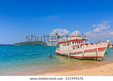 Fishing boat parked on a beach with children playing water jump, with a sky background.