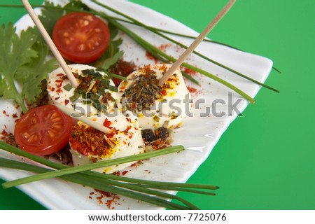 pieces of cheese with fresh vegetables and spices on green background