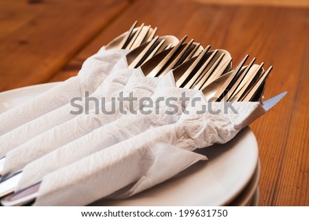 Spoons Forks and Knifes in Napkin Papers on Dishes.