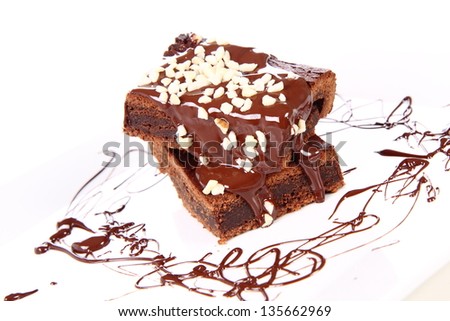 Slices of a brownie on a plate covered with chocolate and nuts
