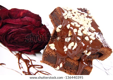 Slices of a brownie on a plate covered with chocolate and nuts, decorated with a dried rose flower