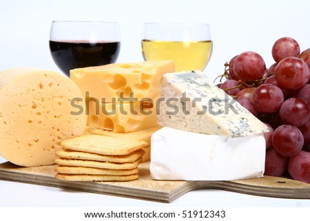 Various types of cheese (swiss, yellow, brie, blue cheese) with red and white wine, red grapes and crackers in close up on white background