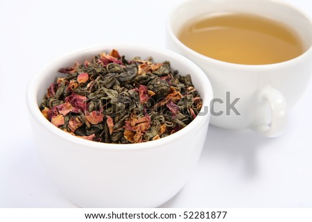 Bowl filled with dried green tea leaves and rose petals and a cup of green tea