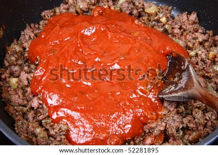 Spaghetti bolognese sauce being fried on a pan with a wooden ladle