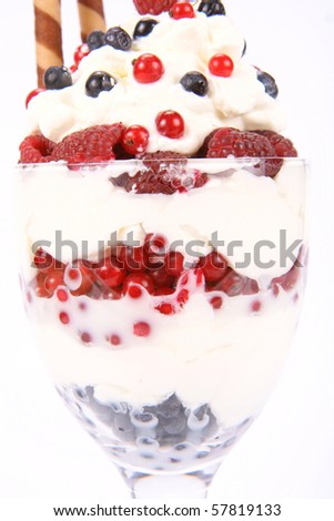 Whipped cream with raspberries, red currants and blue berries in a glass cup, decorated with a wafer tube in close up