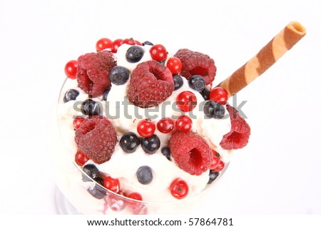Whipped cream with raspberries, red currants and blue berries in a glass cup, decorated with a wafer tube in close up